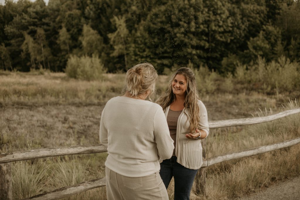 Twee vrouwen praten bij een houten hek in de natuur.